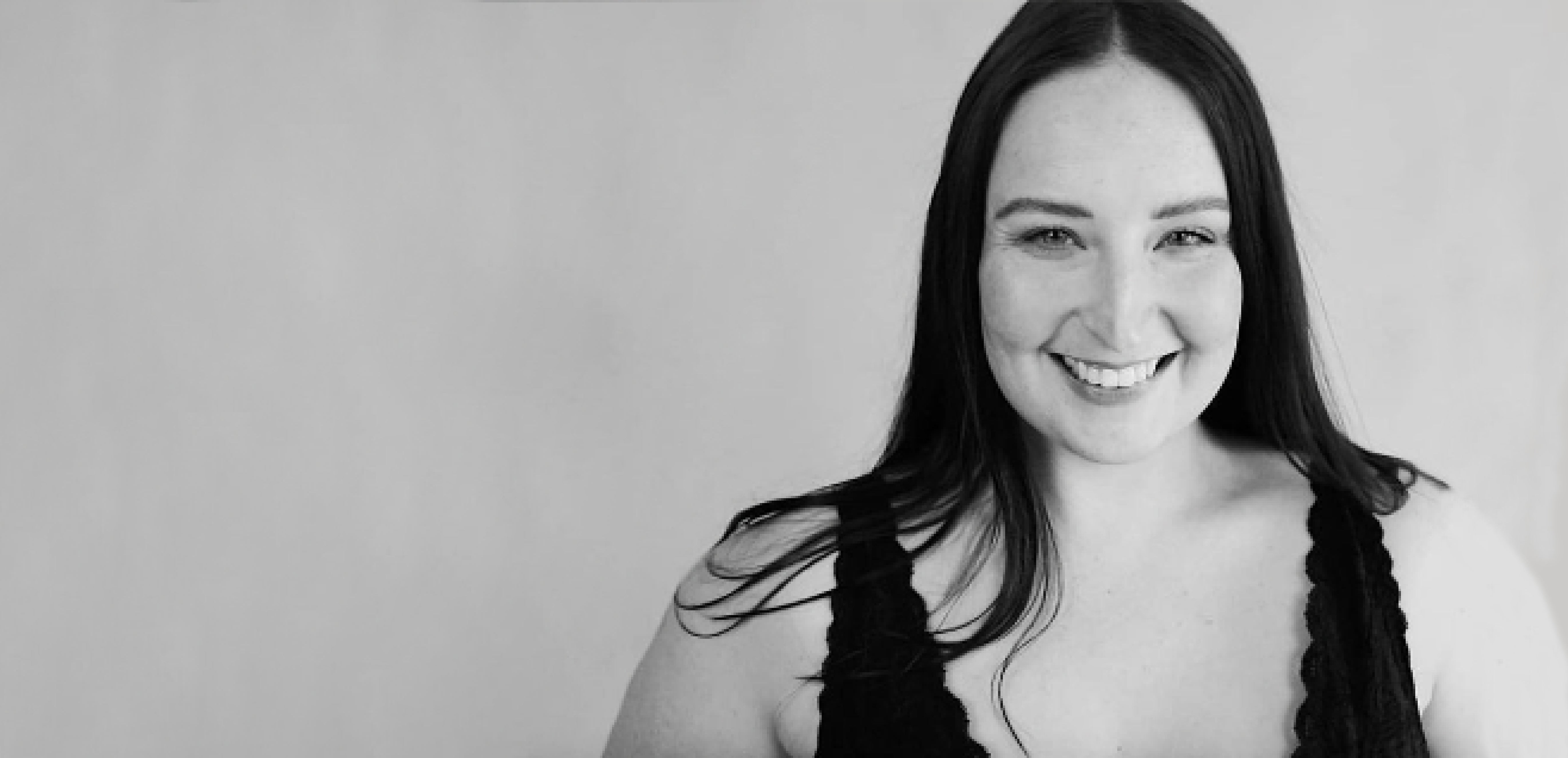 Alt text: Black & White image with Lucy Richardson off centre to the right & smiling brightly and wearing a black top.